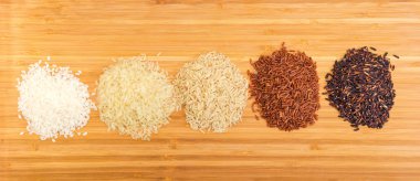 Bambu kesme tahtası ham kısa taneli beyaz ve kaynatılmış pirinç, uzun taneli pirinç kahverengi, kırmızı ve siyah yığınları ile üstten görünüm