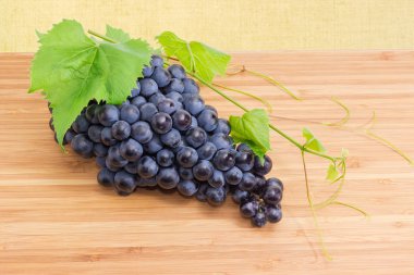 Olgun masa mavi üzüm kümesinde küçük asma kök yaprakları ve dalları bambu ahşap yüzeyi ile