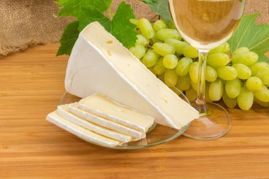 Dilimler ve brie peyniri bir bambu ahşap yüzeyde beyaz şarap ile arka plan beyaz üzüm ve cam parçası küme üzerinde cam daire üzerinde parça