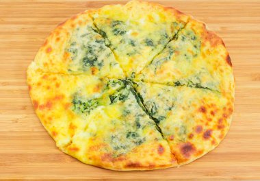 Sektör üstünde ahşap bambu kesme tahtası yakın çekim yuvarlak khachapuri peynir ve yeşillik ile bölünmüş