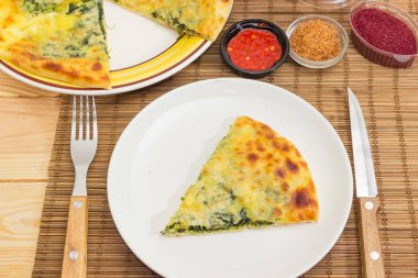 Yemek parçası kısmen khachapuri, diğer çanak, çatal, bıçak ve baharat bambu yer mat yakın çekim üzerinde üzerinde bir dilim dilimlenmiş