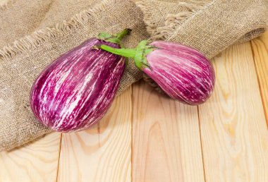 Olgun çiğ mor beyaz çizgili patlıcan olarak da bilinen bir çuval bezi ve açık renkli ahşap yüzey üzerinde patlıcan Graffiti ile