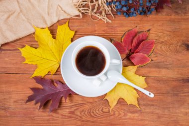 Beyaz taze yapılmış kahve fincan tabağı ile seramik kaşık ve şeker sonbahar yaprakları ve kadın eşarp ile eski rustik ahşap masa üzerinde yukarıdan