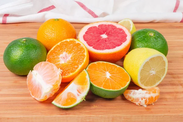 Whole, halves and slices of orange, mandarin orange, green tangerine, lemon and red grapefruit on a bamboo wooden surface