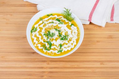Yeşiller, susam ve ekşi krema bir bambu ahşap yüzeyde beyaz kase kabak çorbası püre kırmızı mercimek ile süslenmiş