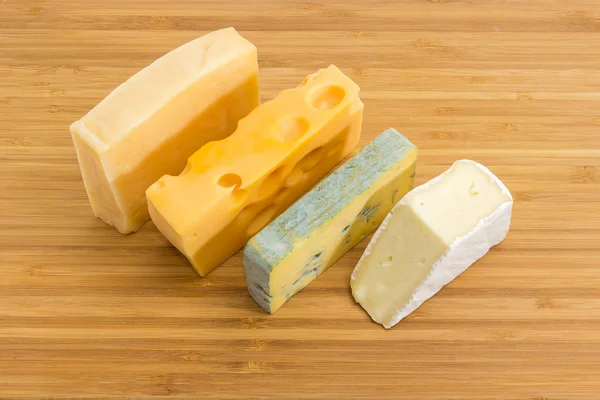 Pieces of blue cheese, brie, medium-hard Swiss and hard cheese on the bamboo cutting board