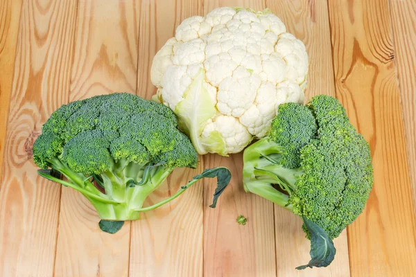 Top view of the two heads of fresh broccoli and head of cauliflower close-up on the light colored wooden rustic table