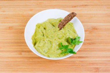 Guacamole mix ham avokado maydanoz dal ve kahverengi ekmek bir bambu ahşap yüzeyde beyaz kase süslenmiş ile hazırlanan