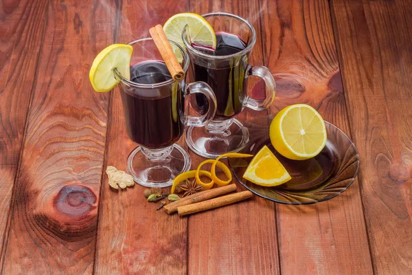 Mulled wine in two glass mugs with slice of lemon and mulling spices for its preparation on dark colored wooden rustic table