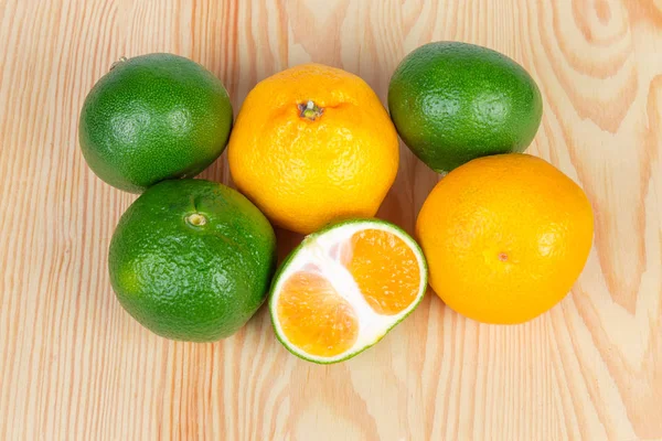 Bir açık renkli ahşap yüzeyde Bütün Konfit yeşil mandalina ve sıradan mandarin portakal ve yeşil mandalina yarısı üstten görünüm