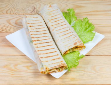 Bir gözleme içinde sarılmış ve ızgara Shawarma, açık renkli ahşap rustik Masa kare beyaz bir tabak üzerinde marul yaprakları