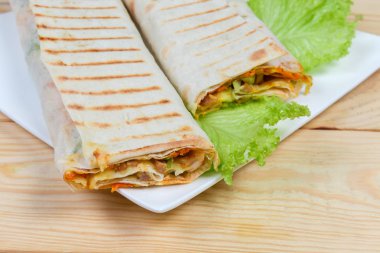 Bir gözleme içinde sarılmış ve ızgara shawarma iki bölümünü parçası, bir tabak üzerinde seçici odak, açık renkli ahşap rustik masa üzerinde marul yaprakları