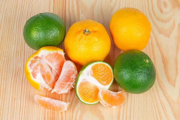Bir açık renkli ahşap yüzeyde bütün, yarım ve olgun yeşil mandalina ve sıradan mandarin portakal segmentlerinin üstten görünüm