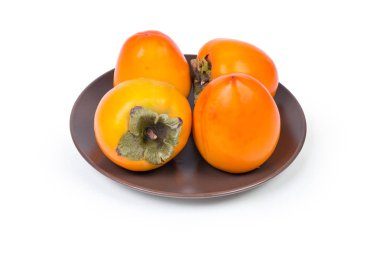 Several fresh ripe whole persimmon fruits on a brown dish on white background clipart