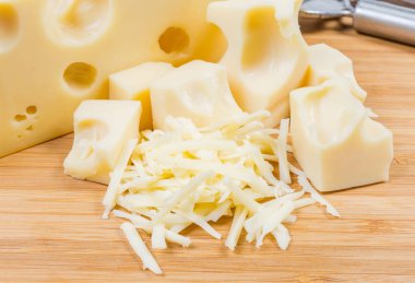 Grated Swiss-type cheese on background of slices of the same cheese on a bamboo wooden cutting board close-up