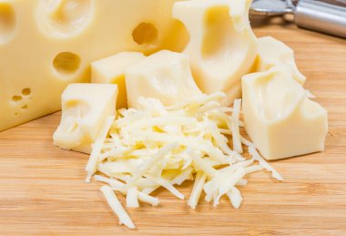 Grated Swiss-type cheese on background of slices of the same cheese on a bamboo wooden cutting board close-up clipart
