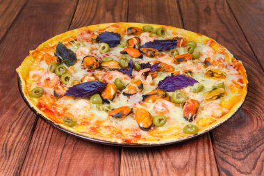 Zeytin, dekore edilmiş bir fırın tepsi üzerinde koyu renkli rustik ahşap masa yakın çekim seçici odak, Fesleğenli deniz ürünleri ile yuvarlak pizza, pişmiş