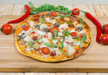 Tavuk eti, sosis, düğme mantar, domates ve yeşillik ve sebzeler arasında roka ile pişmiş yuvarlak pizza üstten görünüm ahşap bambu kesme tahtası