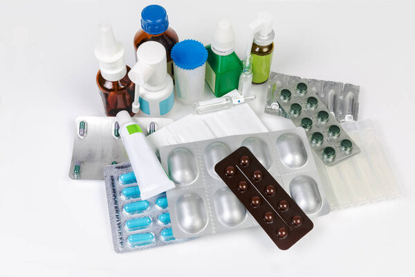 Various pills, ointment, sprays, powdery and liquid medicines in different types of packaging on a white table