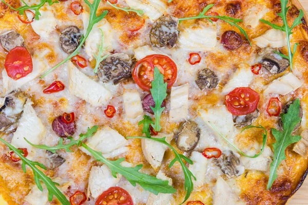Background of cooked pizza with chicken meat, frankfurters, button mushrooms, tomatoes and arugula. Fragment close-up