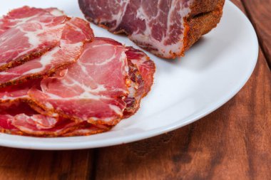 Dilimler ve koyu renkli ahşap rustik masa yakın çekim seçici odak, kurutulmuş domuz eti boyun parça geri kalanı ile beyaz yemek parçası