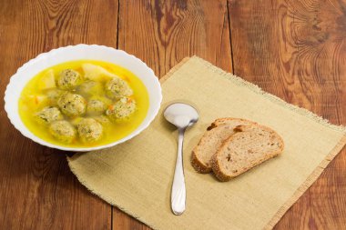 Çorba tavuk köfte beyaz kase, kaşık ve eski koyu renkli rustik ahşap masa Tekstil peçeteye kahverengi ekmek dilimleri ile