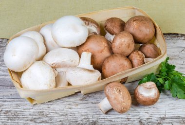 Küçük ahşap sepet ve maydanoz eski bir kırık ahşap yüzey üzerinde ekili ham beyaz ve kahverengi düğme mantar