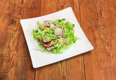 Sebze salatası dilimlenmiş taze genç lahana, kırmızı turp yapılan ve eski ahşap rustik Masa kare beyaz çanak üzerinde yeşil soğan kıyılmış