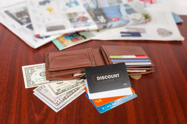 プラスチックの割引カードを開く茶色の革財布と金商品カタログの背景をぼかした写真の赤い木製のテーブルに — ストック写真