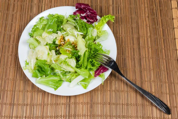 Salad of leaves of green and red lettuce varieties with mustard salad dressing on dish with fork on a bamboo table mat