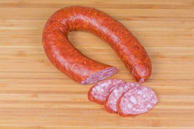 Top view of the partly sliced boiled-smoked pork sausage known as bologna sausage in natural casing curtailed by a ring on the wooden bamboo cutting board clipart