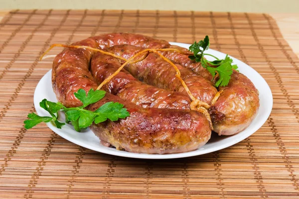 Fresh baked homemade turkey meat sausage curtailed by a rings, tied with twine and  decorated with parsley on dish on a bamboo table mat close-up at selective focus