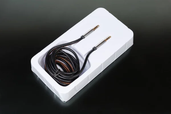 High-fidelity analog shielded audio cable with gold-plated stereo connectors mini jack in plastic packaging on a dark matt surface