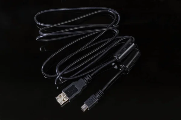 Black cable with plugs USB standard A and mini-USB standard B at the edges on a dark reflective surface