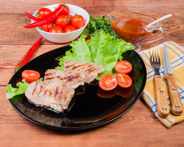 Bifes de porco grelhados com legumes em prato, garfo e faca — Fotografia de Stock
