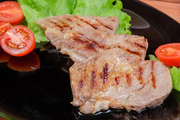 Grilovaný šťavnatý vepřové steaky se zeleninou na černé nádobí closeup — Stock fotografie