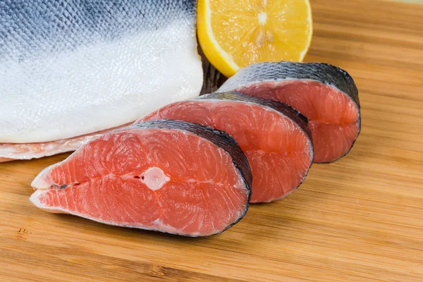 Неприготовленные стейки лосося против кусочка рыбы и лимона — стоковое фото