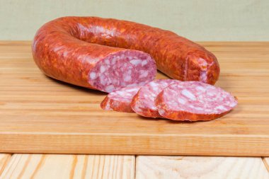 Partly sliced pork bologna sausage on a wooden cutting board clipart