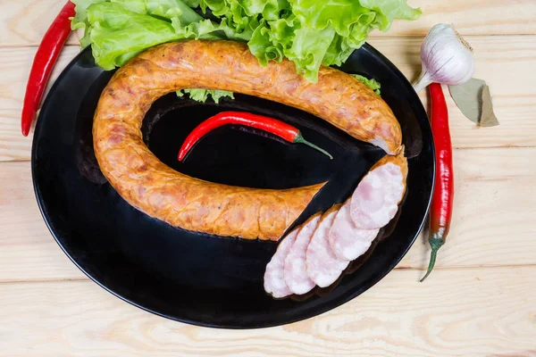 Partly sliced bologna sausage on dish among spices and vegetable