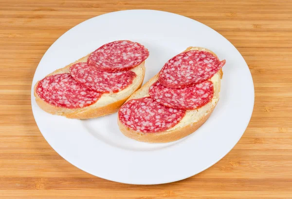 Sanduíches abertos com salame em prato em uma superfície de madeira — Fotografia de Stock