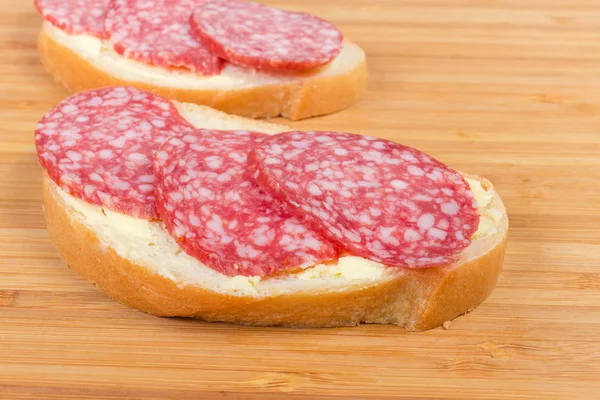 Sanduíches abertos com salame na placa de corte de bambu close-up — Fotografia de Stock