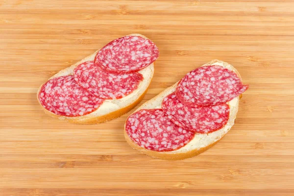 Sanduíches abertos com salame em uma placa de corte de bambu de madeira — Fotografia de Stock