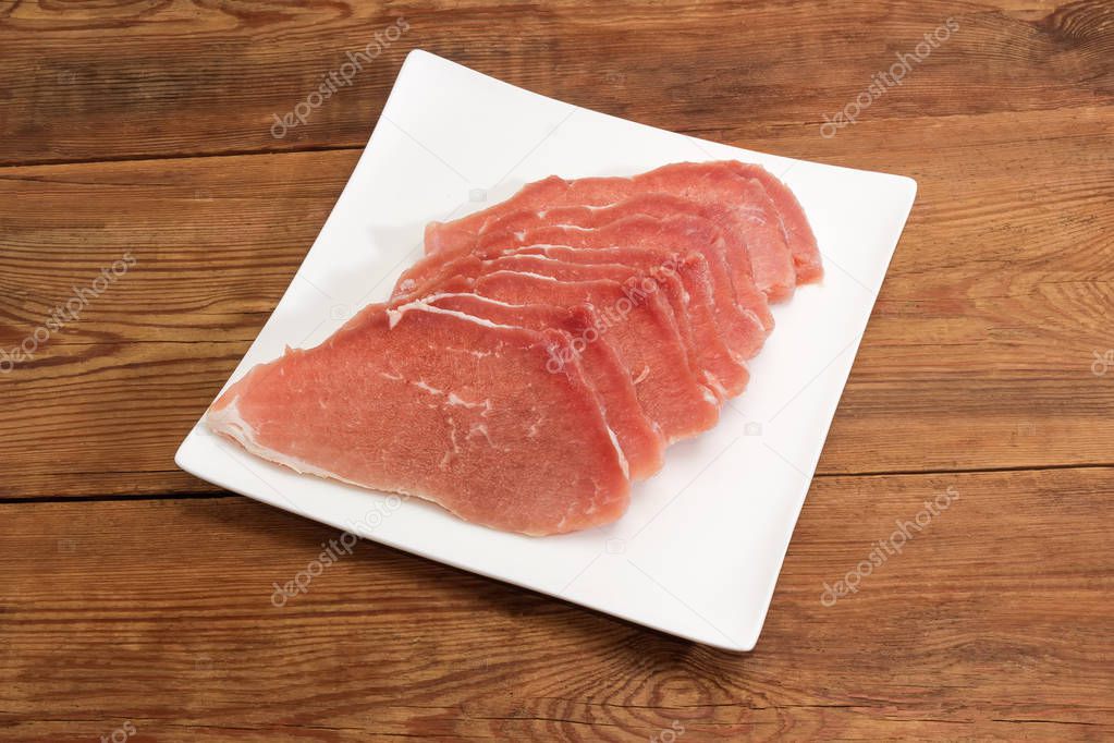 Uncooked defrosted pork slices on the square dish