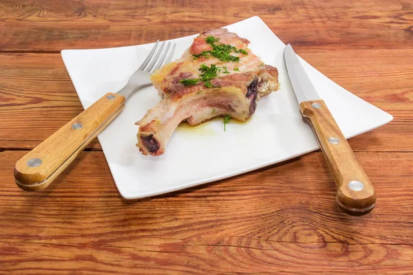 Grilled pork loin on bone on dish, fork and knife — Stock Photo, Image