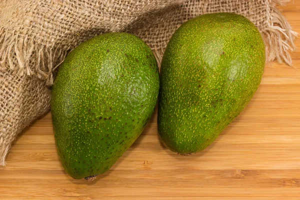 Twee hele groene avocado vruchten op een houten oppervlak — Stockfoto