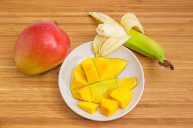 Tam ve hazırlanmış mango, kısmen soyulmuş muz ahşap yüzeyde.