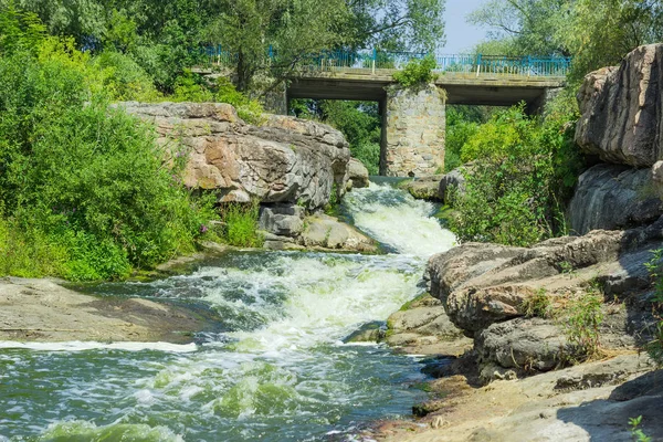 Malý vodopád na řece tekoucí pod kamenným mostem — Stock fotografie