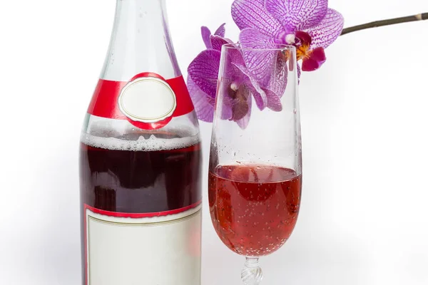 Bottiglia e bicchiere da vino di spumante rosso contro orchidea primo piano — Foto Stock