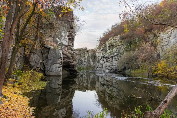 Overhanging rocks over calm river in canyon at late autumn
