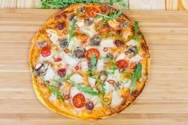 Kesme tahtasıüzerinde tavuk, mantar, domates ve arugula ile Pizza